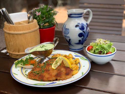 Schnitzel mit Beilagen, Kräutersoße, Salat und einer blauen Krug auf einem Holztisch.