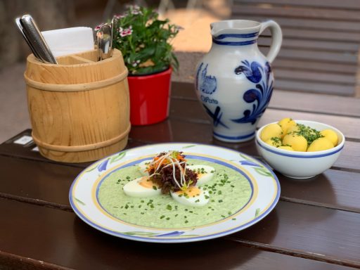 Grüne Soße mit Gemüse und Kräutern, neben einer Schüssel mit Kartoffeln und einem Krug.