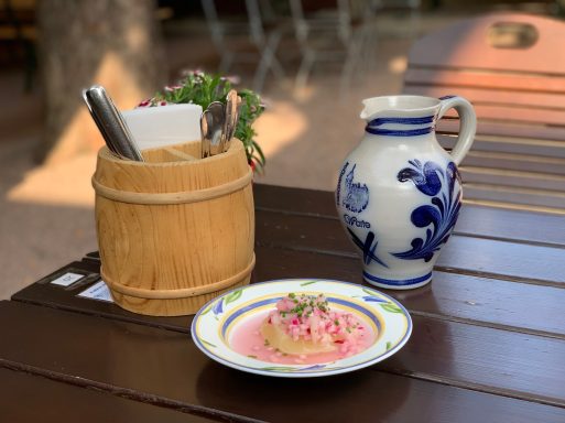 Teller mit rosa Vorspeise, Bullenkaraffe und Besteck in einem Holzbehälter.