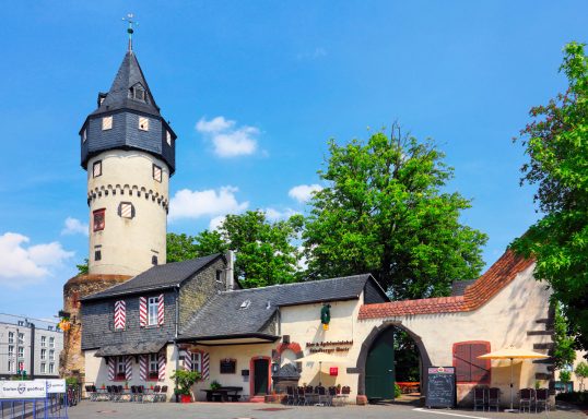 Historisches Gebäude mit Turm und grünen Bäumen im Hintergrund.